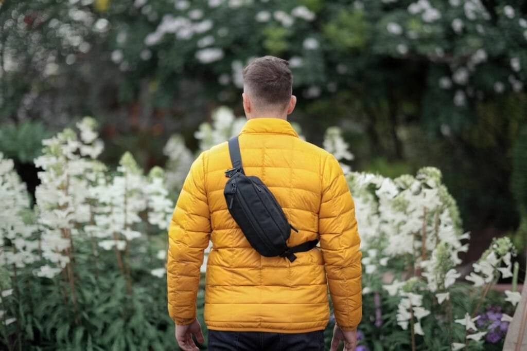 Best sling bag Aer City Sling 2 showcased on person in yellow jacket amid lush garden blooms.
