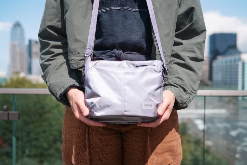 Best sling bag Bellroy Laneway Sacoche in urban city setting with modern high-rise backdrop.