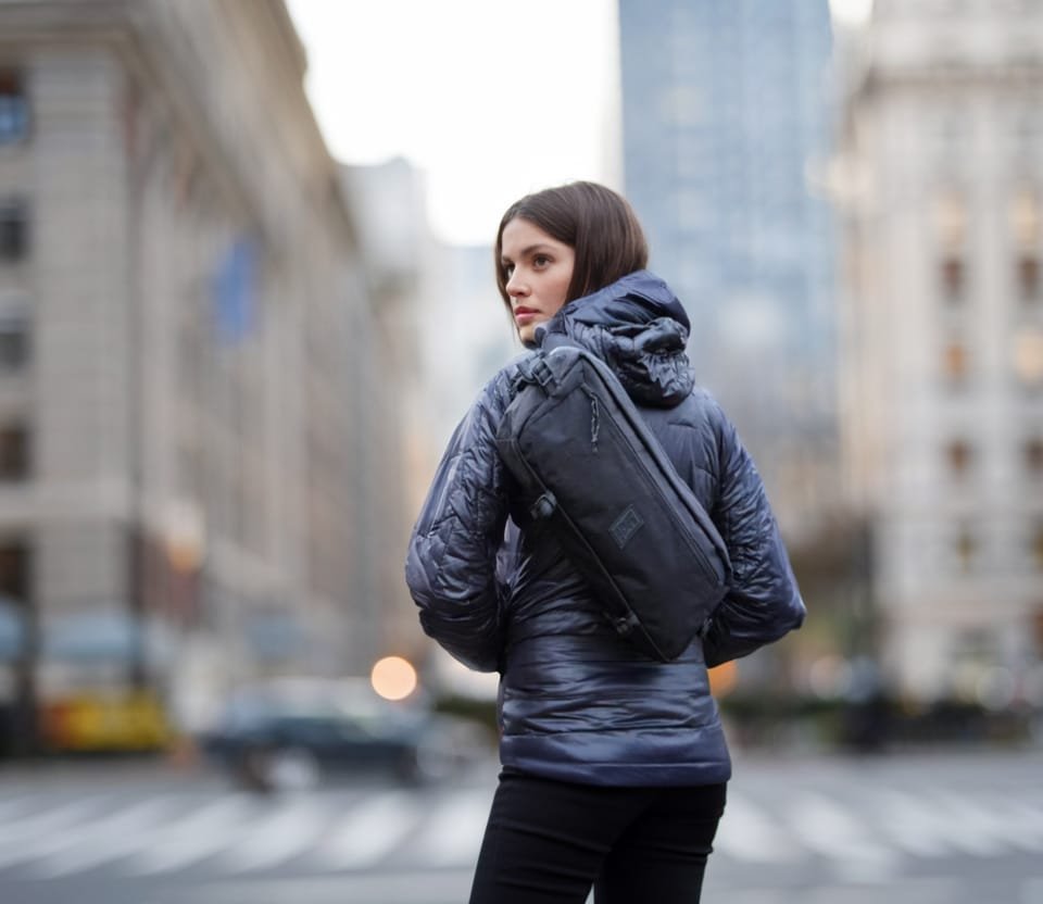 Best sling bag Chrome Industries Kadet model on urban street with cityscape background in fall.