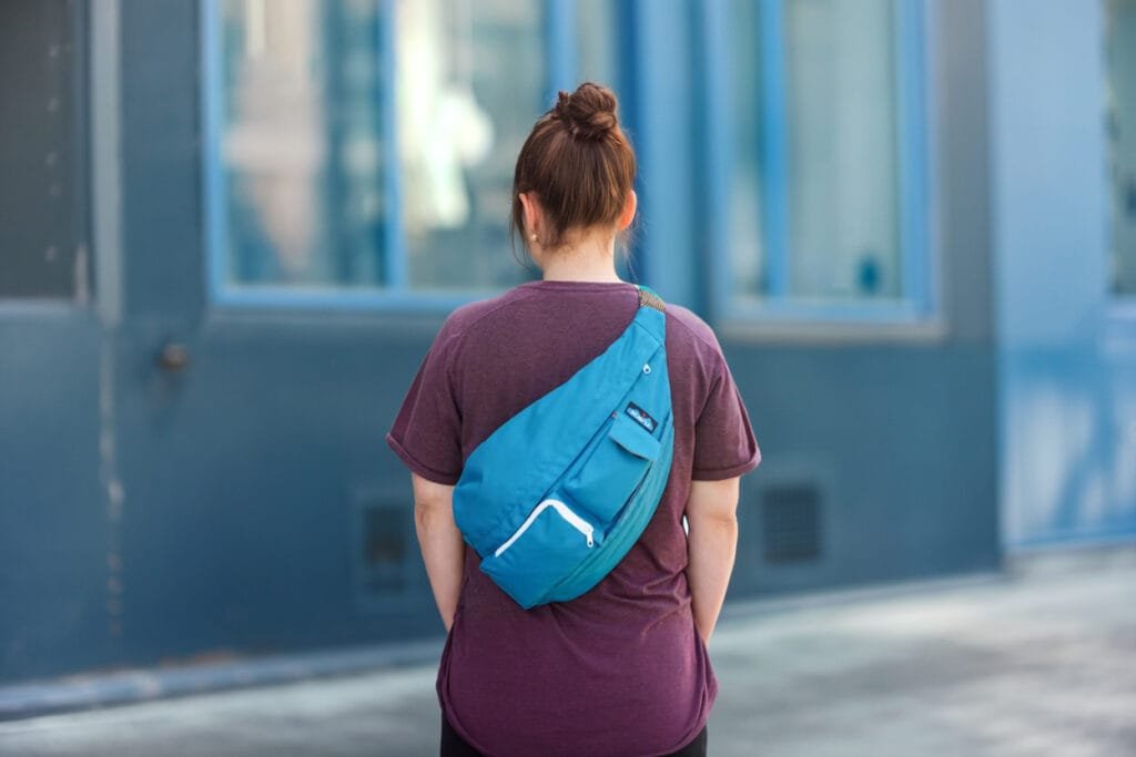 Best Sling Bag Kavu Rope Sling in urban setting with modern architecture and vibrant blue bag.