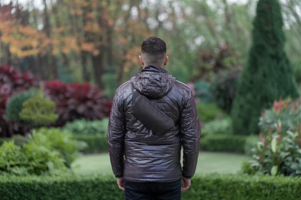 Best sling bag lifestyle scene with person in brown puffer jacket enjoying serene garden.