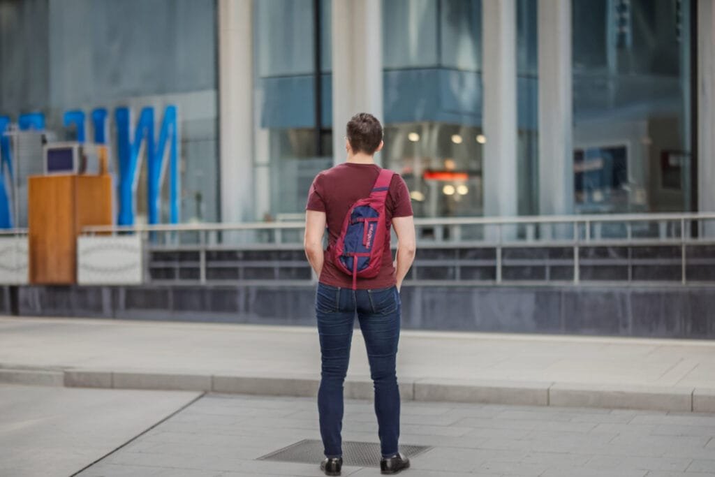 Best sling bag review featuring young man with Patagonia Atom Sling, urban city backdrop, modern architecture.