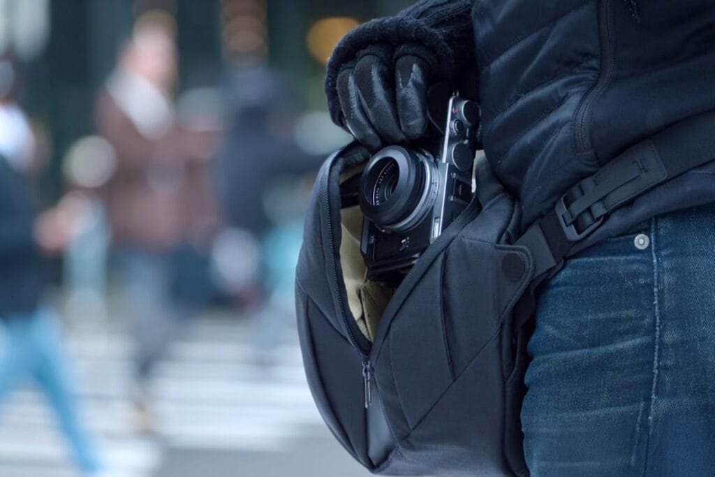 Best sling bag Peak Design Everyday Sling holds camera in urban setting with gloved grip, blurred background.