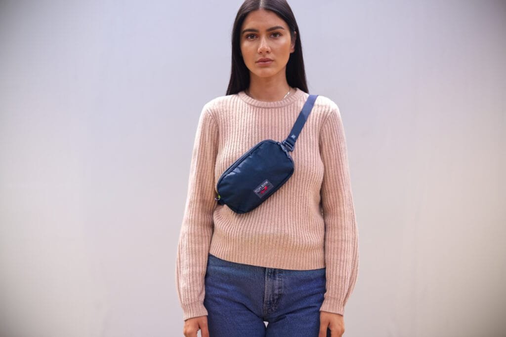 Best sling bag Tom Bihn Bantam with crossbody style on woman in pink sweater and blue jeans.