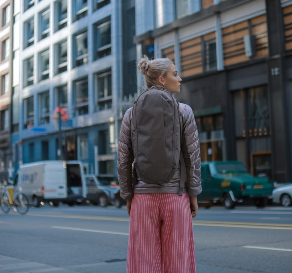 Best travel backpack shown in urban setting with woman wearing light brown jacket and striped pants.