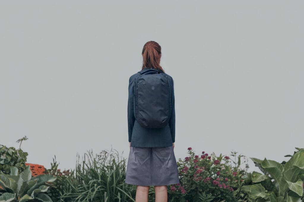 Best travel backpack Tortuga, central figure with backpack amidst serene nature and neutral backdrop.