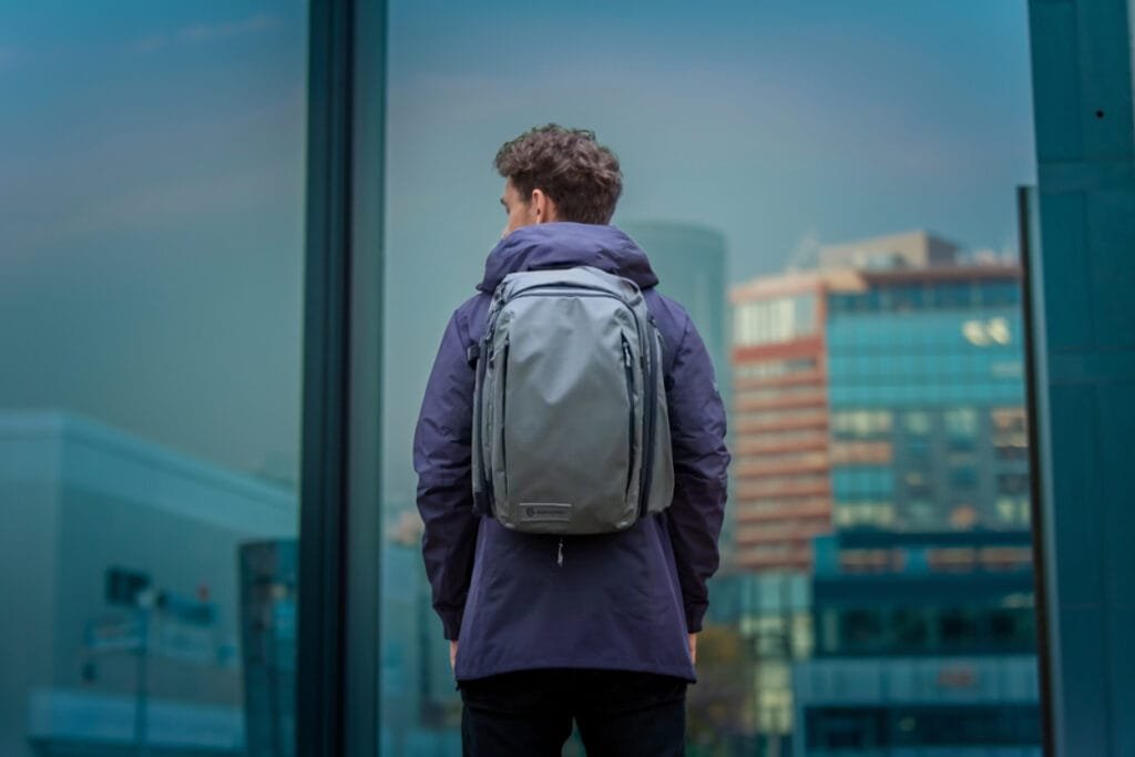 Best travel backpack Wandrd Transit in urban cityscape with reflective glass building and casual style.