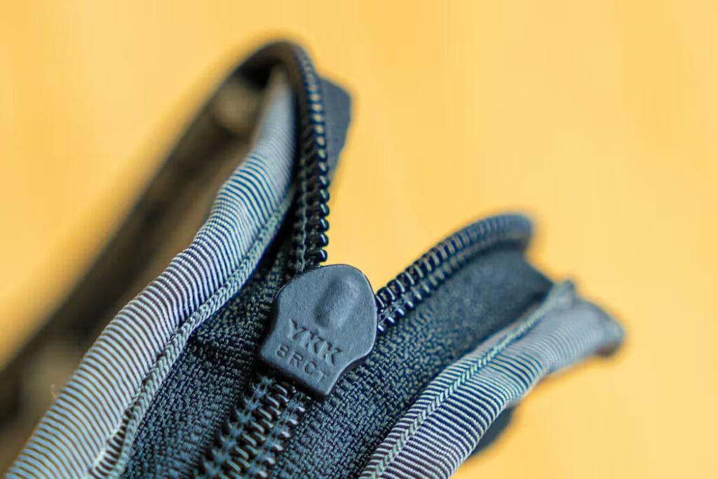 Best travel backpack zipper closeup showing detailed plastic teeth and ergonomic pull against warm background.