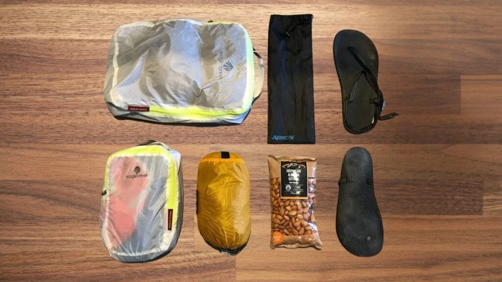 Goruck Gr2 40l travel essentials shown on a wooden floor: bags, flip-flops, snack, and jacket.