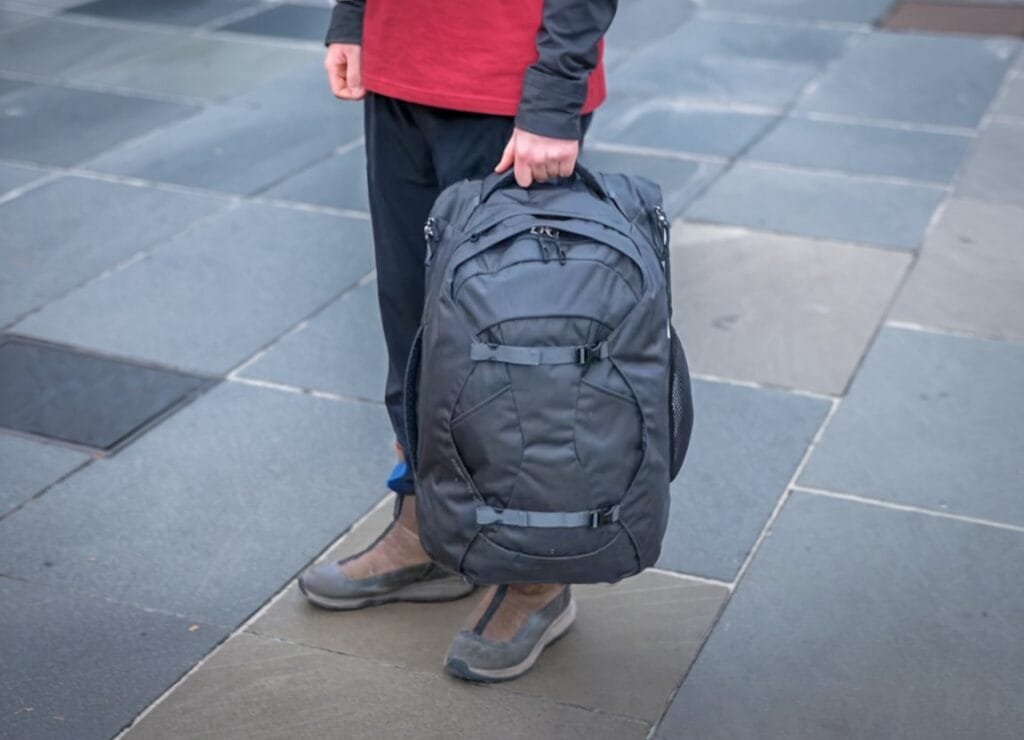 Osprey Farpoint 40 carried by traveler in casual attire on stone-tiled pavement in urban setting.