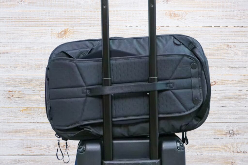 Peak Design Travel Backpack on rolling luggage, showcasing sleek black design and travel efficiency.